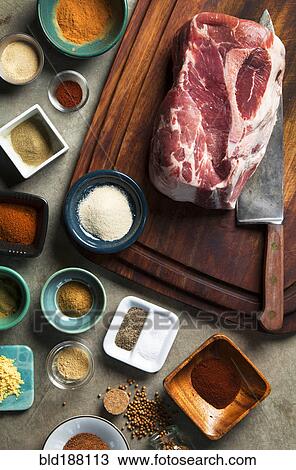 Stock Image - Cutting board with pork shoulder and variety of spices. Fotosearch