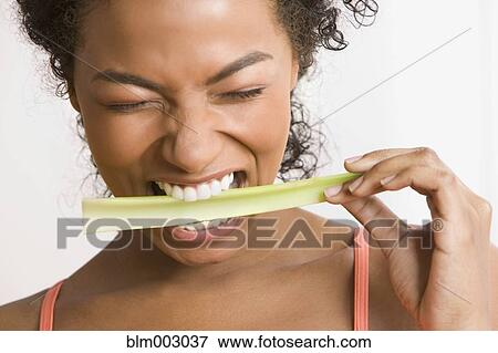 Stock Photo - Disgusted African woman biting celery. Fotosearch