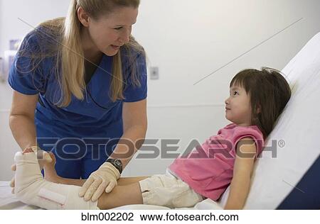 Stock Image - Doctor examining girl's leg in cast. Fotosearch