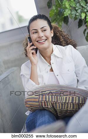 Stock Photography - Dominican woman talking on cell phone on sofa. Fotosearch