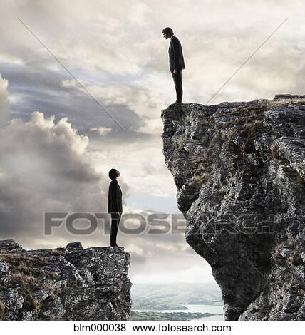 Stock Photo - European businessmen on cliffs looking at each other. Fotosearch