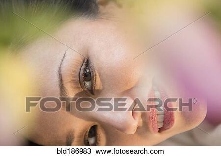 Stock Image - Face of smiling woman obscured by flowers. Fotosearch