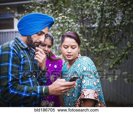 Stock Photography - Family in traditional Indian clothing using cell phone. Fotosearch