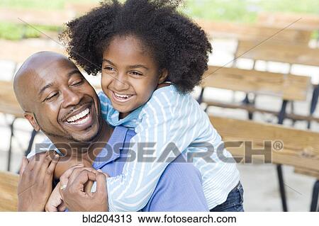 Stock Image - Father and daughter smiling on park bench. Fotosearch