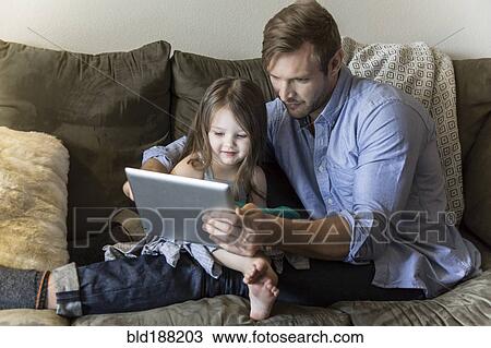 Stock Image - Father and daughter using digital tablet on sofa. Fotosearch