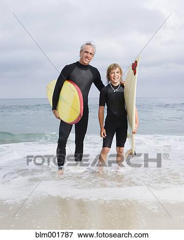 Stock Photo - Father and son holding surfboards at beach. Fotosearch