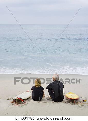 Stock Photography - Father and son sitting on beach with surfboards. Fotosearch