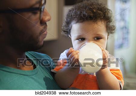 Stock Photo - Father helping baby drink bottle in kitchen. Fotosearch