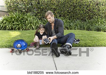 Stock Photography - Father helping daughter use knee pads and skateboard. Fotosearch