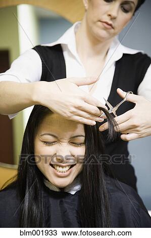 Stock Image - Female hair stylist cutting woman's hair in salon. Fotosearch