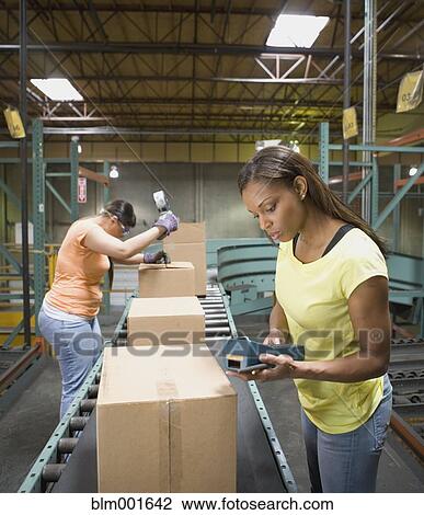 Stock Image - Female warehouse workers checking boxes on conveyor belt. Fotosearch