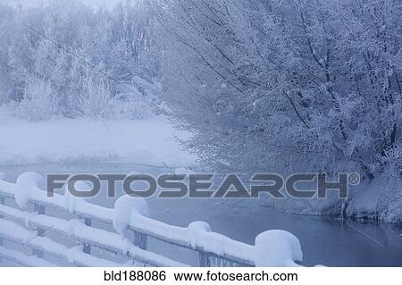 Stock Photograph - Fence and snowy trees over remote river. Fotosearch