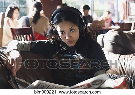 Stock Image - Filipino woman listening to headphones in coffee shop. Fotosearch