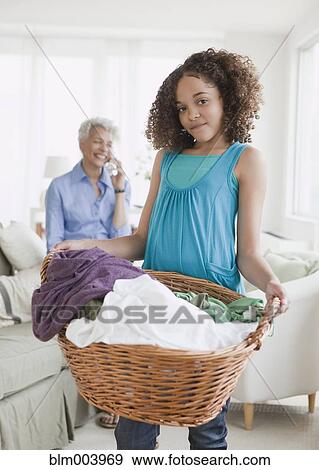 Stock Photo - Girl holding laundry basket with grandmother on phone in background. Fotosearch