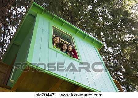 Stock Image - Girls leaning out tree house window. Fotosearch