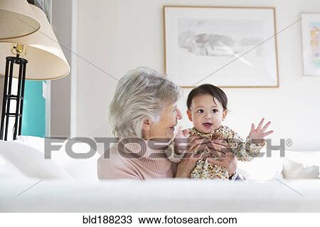 Stock Image - Grandmother and granddaughter hugging on sofa. Fotosearch