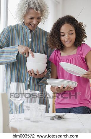 Stock Image - Grandmother and granddaughter setting table. Fotosearch