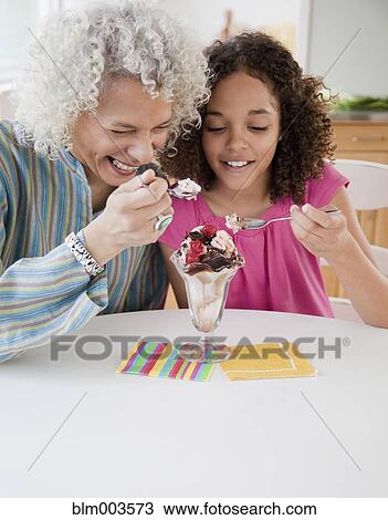 Stock Image - Grandmother and granddaughter sharing ice cream sundae. Fotosearch