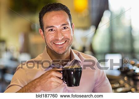 Stock Image - Hispanic barista drinking coffee in coffee shop. Fotosearch