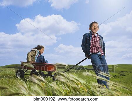 Stock Image - Hispanic brother pulling sister in wagon. Fotosearch