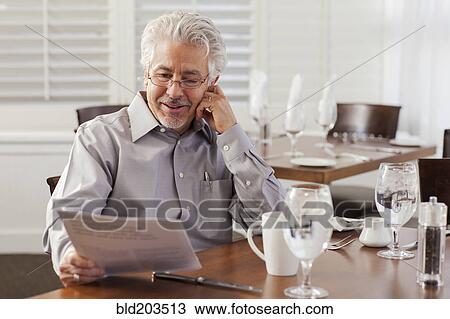 Stock Image - Hispanic businessman reading papers in cafe. Fotosearch