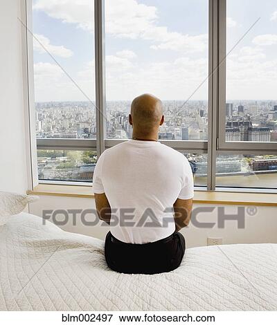 Stock Photo - Hispanic businessman sitting on edge of bed. Fotosearch