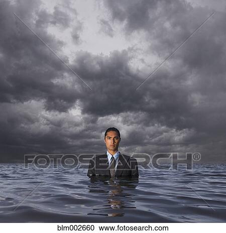 Stock Image - Hispanic businessman standing in water. Fotosearch