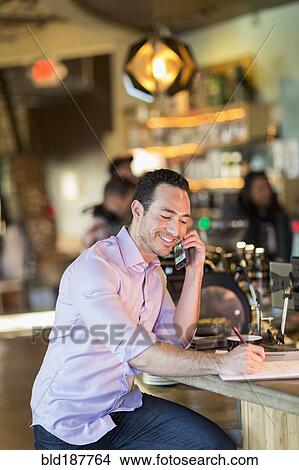 Picture - Hispanic businessman talking on cell phone in coffee shop. Fotosearch