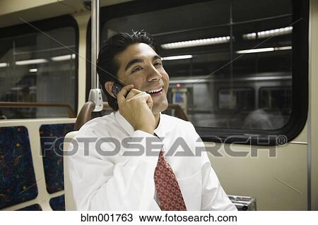 Stock Image - Hispanic businessman talking on cell phone on subway. Fotosearch