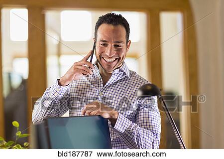 Stock Photo - Hispanic businessman talking on cell phone in office. Fotosearch