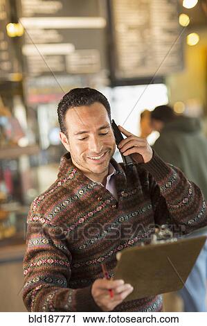 Stock Image - Hispanic businessman talking on telephone in coffee shop. Fotosearch