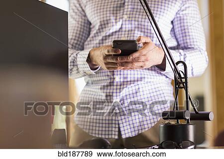 Stock Photo - Hispanic businessman using cell phone in office. Fotosearch