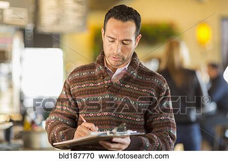 Stock Image - Hispanic businessman writing in coffee shop. Fotosearch