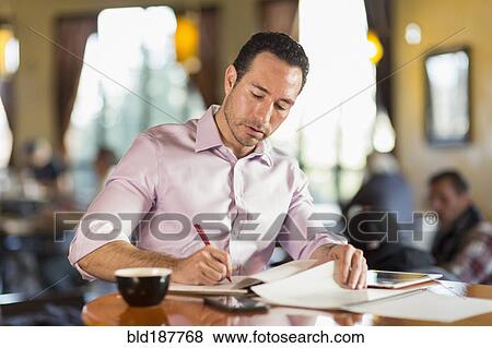 Stock Photo - Hispanic businessman writing in coffee shop. Fotosearch