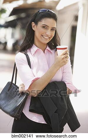 Stock Image - Hispanic businesswoman holding take out coffee. Fotosearch