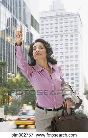 Stock Photo - Hispanic businesswoman in city hailing taxi. Fotosearch