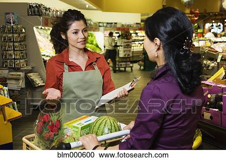 Stock Image - Hispanic clerk helping shopper in grocery store. Fotosearch