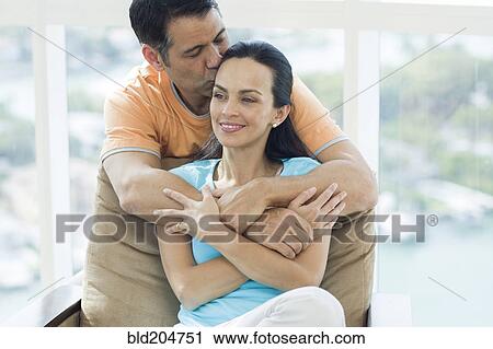Stock Image - Hispanic couple hugging in armchair. Fotosearch