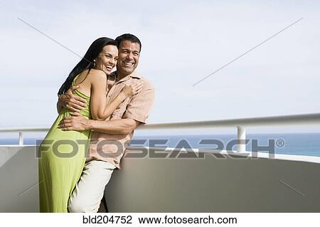 Stock Image - Hispanic couple hugging on boat deck. Fotosearch