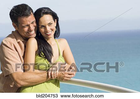 Stock Image - Hispanic couple hugging on boat deck. Fotosearch