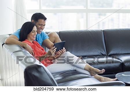 Stock Photo - Hispanic couple using tablet computer on sofa. Fotosearch