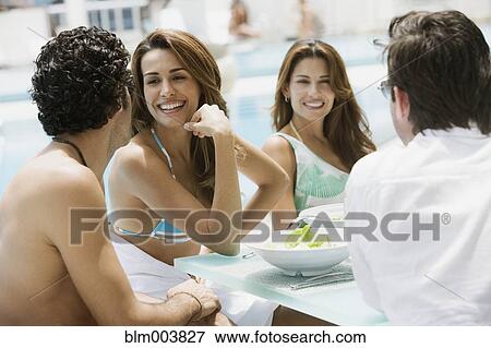 Stock Photo - Hispanic couples eating lunch poolside. Fotosearch