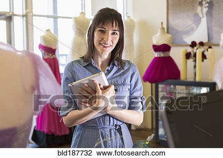 Stock Image - Hispanic entrepreneur holding digital tablet in bridal shop. Fotosearch