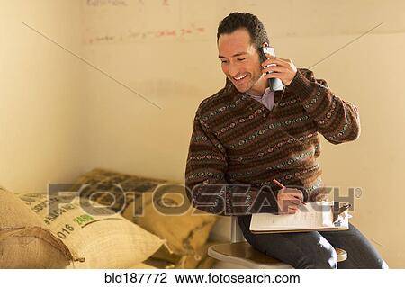 Stock Image - Hispanic entrepreneur talking on telephone in store. Fotosearch