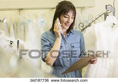 Stock Photograph - Hispanic entrepreneur talking on telephone in bridal shop. Fotosearch