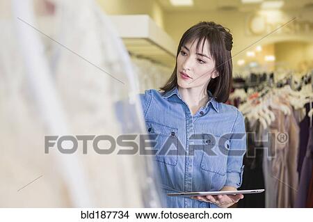Picture - Hispanic entrepreneur using digital tablet in bridal shop. Fotosearch