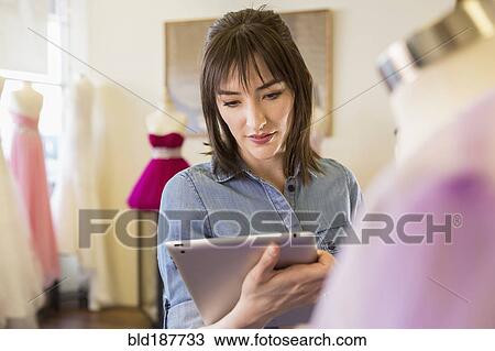 Stock Image - Hispanic entrepreneur using digital tablet in bridal shop. Fotosearch