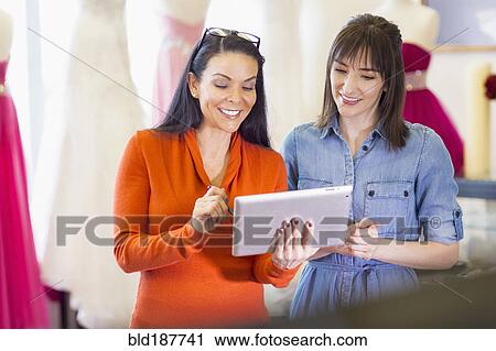 Stock Image - Hispanic entrepreneurs using digital tablet in bridal shop. Fotosearch