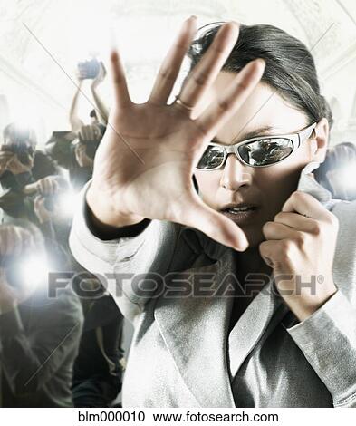 Stock Image - Hispanic female celebrity shielding face from photographers. Fotosearch