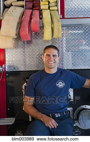 Stock Photo - Hispanic fireman leaning against fire engine. Fotosearch